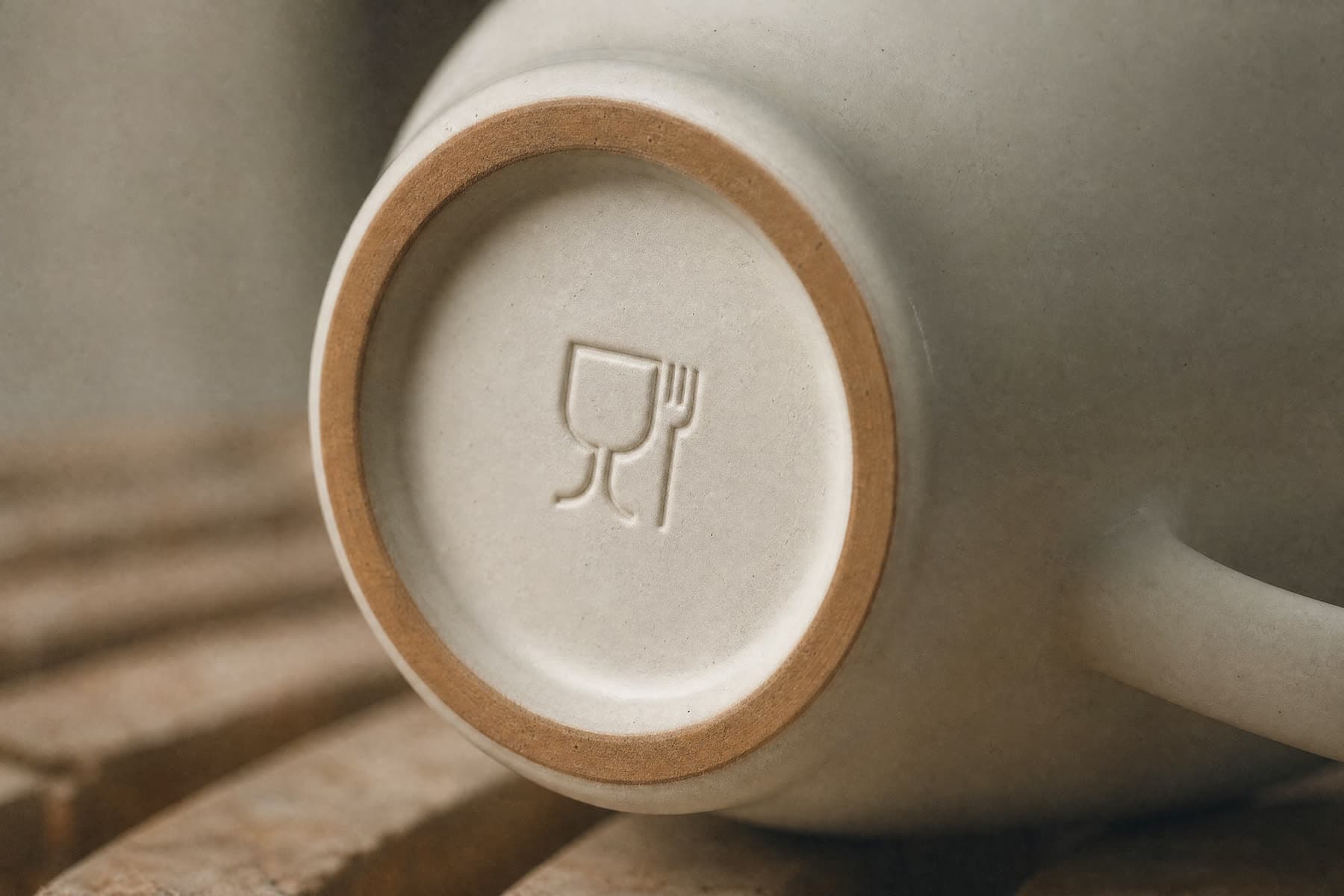 The underside of a porcelain cup showing an impressed wine glass and fork food contact symbol